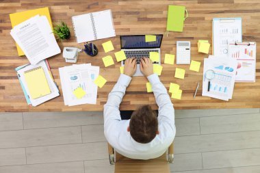 Ofis çalışanı bilgisayarda çalışıyor. Masasında notlar ve şemalı belgeler var. Yönetici birçok görevi aynı anda üst görünümde gerçekleştirir