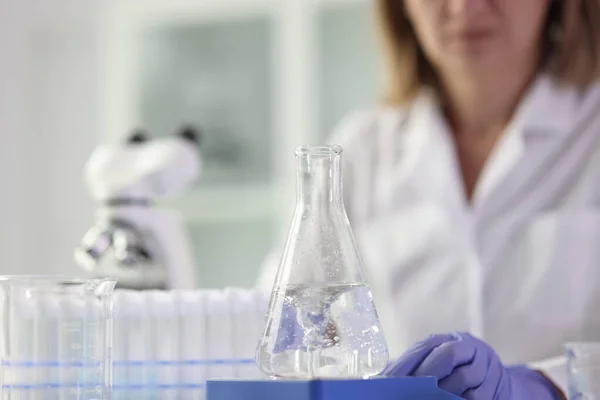 女性の化学者は 試験管でテーブルに座って明確な液体でフラスコ科学研究を行います 研究室のアシスタントは ソリューションの特性を調べる — ストック写真