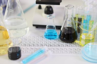İçinde sıvı örnekleri olan mataralar ve tüpler laboratuvar ofisindeki kimyasal elementlerin periyodik tablosuyla masada duruyor. Ekipmanlı tıbbi uygulamalar için araştırma kavramı