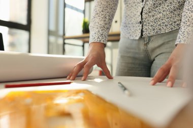 Kadın emlakçı, ofisteki ahşap masaya bina çizimi yaparak büyük kağıtları açıyor. Kadın mimar emlak projesiyle çalışmaya hazırlanıyor