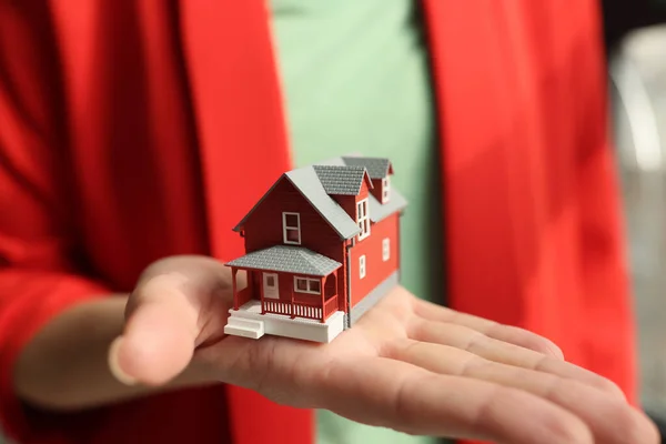 Woman realtor in jacket holds small house model. Red building design in copy on employee palm. Concept of real estate purchase offer