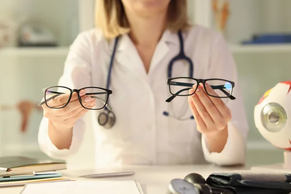 女性の観光客は手に持っている眼鏡モデルを比較します 女性医師は クリニックの前提でテーブルに座って可視性調整のための患者オプションを提供しています — ストック写真