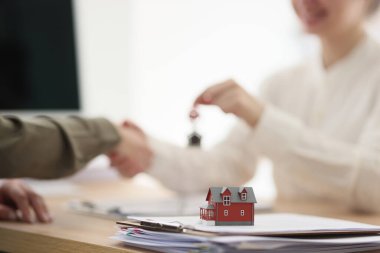 Emlakçı yeni evin anahtarını şirket ofisindeki masada oturan alıcıya devrediyor. Resmi kurum tarafından gayrimenkul satışı