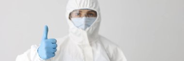 Portrait of woman in protective respirator and white coverall showing thumb up sign. Smart scientist. Female chemist in eyeglasses. Science and lab concept