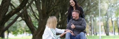 Portrait of women friends walking with disabled man in wheelchair in park. Disability and healthcare concept