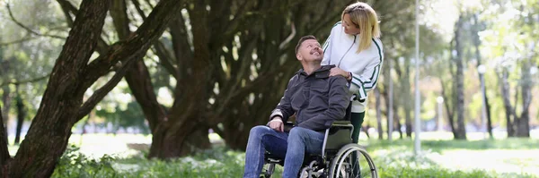 stock image Portrait of woman walking with disabled man in wheelchair in park. Couple in love. Disability and healthcare concept