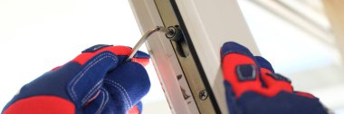 Close-up of repairman hands in gloves adjusting locks of new pvc windows with special key. Installation of plastic windows