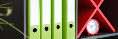 Close-up of shelves with office folders with documents and red alarm-clock. Archive and data. Business and workplace organization concept