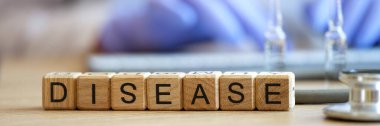 Close-up of word disease made of wooden blocks in raw on table. Doctor typing prescription. Diagnostics of illness, treatment and healthcare concept