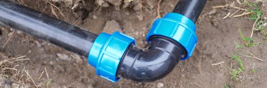 Close-up of elbow fitting and black pvc pipes at bend in trench outdoors. Plumbing water drainage installation. Underground irrigation system concept