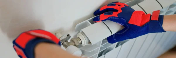 Close-up of male plumber hands in protective gloves installing heating radiator in apartment or house. Builder installs new hot water central heating system using wrench