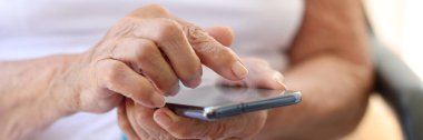 Close-up of old grandmother holding modern cellphone in hands. Woman using smartphone. Communication with relatives, old age and senility concept