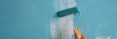 Close-up of decorator hand painting walls in blue color with roller. Interior decorating. Repair and renovation concept