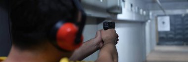 Kulaklıklı bir adamın hedefe ateş edişine yakın çekim. Atış talimi atış poligonunda. Aşırı hobi konsepti