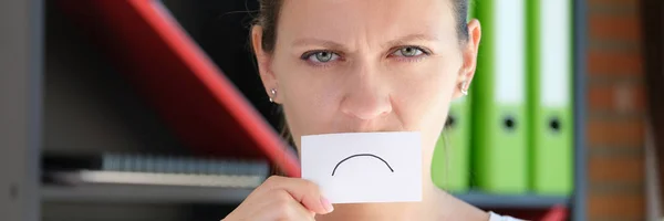 Portrait of woman covering face with paper sad emoticon symbol. Upset face, unhappy emoji, emotion expression concept