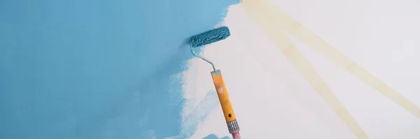 stock image Close-up of decorator painting wall in blue color and using scotch tape and roller. Repair, renovation and creative design of house concept