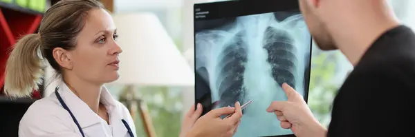 医務室で患者にX線を見せる女性医師 脊髄損傷の説明 骨疾患治療 放射線スキャン後の相談を与えます — ストック写真