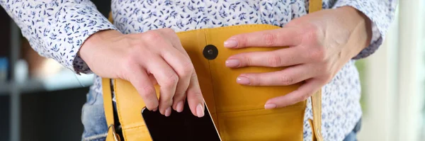 穿着休闲装的女人把她的智能手机放在亮黄色的肩袋里 保障流动电话的安全 — 图库照片