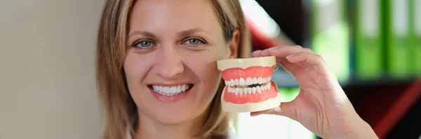 Γυναίκα Οδοντίατρος Χαμογελά Και Δείχνει Τεχνητά Σαγόνια Στο Χέρι Της — Φωτογραφία Αρχείου