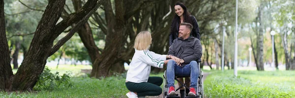 Happy disabled person in wheelchair and two women take care of him in park. Smiling joyful people outdoors, one man with disability in wheelchair.