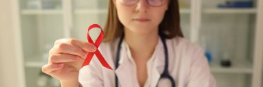 Infectious disease doctor holding red ribbon in his hands on hiv day closeup. Prevention and treatment of AIDS concept
