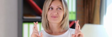 Caucasian woman with emotions of hope on her face stands and gesticulates with crossed fingers. Luck and superstition concept.