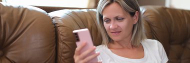 Woman reads messages on her smartphone while sitting on couch. Search for information on the Internet and activity in social networks concept.