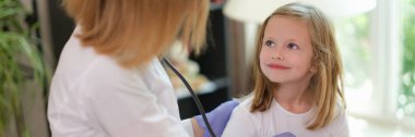 Doctor examines girl in medical office with stethoscope. Medical insurance for children and childrens healthcare concept.