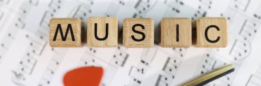 Wooden cubes with letters music and guitar pick on musical notes. Making music and playing the guitar concept.