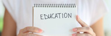 Woman holding notebook with word education on white page close up. Study, learning and school concept.