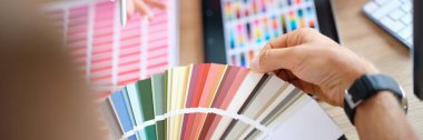 Client chooses color from variety of samples in art studio close up. Manager advises customer on colors for his projects.