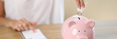 Woman connects electric plug to piggy bank and counting money on calculator. Concept of beginning of saving money and energy.