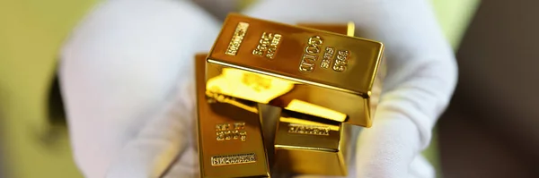 Gold bars in gloved hands close up. Gold price, investment and saving money concept.