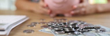 Banknotes and coins on table and blurry woman with piggy bank in background. Concept of saving money and successful investment.