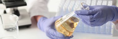 Scientist measuring yellow liquid in flask at chemical laboratory. Biochemistry and pharmaceutical research concept. Scientific researcher work.
