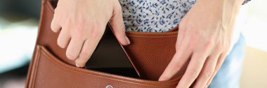 Close-up of female hands hiding smartphone in shoulder bag. Concept of security, protection and anti-theft rules.