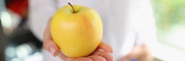 Female nutritionist shows ripe yellow apple on her hand close-up. Healthy food, diet and vegetarian food concept.