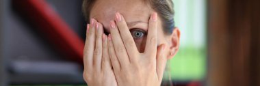 Frightened woman covers her face with her hands and looks through her fingers at camera close-up. Concept of mistake, fear and stress.