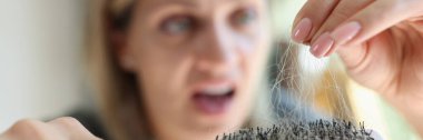 Frightened woman looks at comb with a lot of hair close-up. Concept of hair loss, baldness and disease.