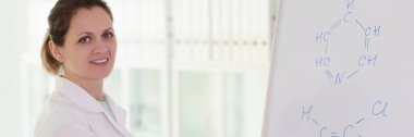 A smiling woman, a scientist writes a chemical formula on a white board, a close-up. Chemistry training, discovery