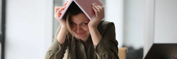オフィスのテーブルの女性は 彼女の頭の上のノートブック クローズアップの下に隠れていました 仕事での過負荷 多くのこと — ストック写真