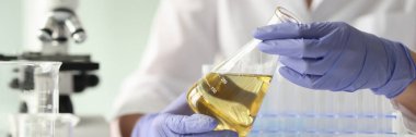 Close-up of scientist woman holding sample with yellow liquid. Testing of sample and laboratory concept