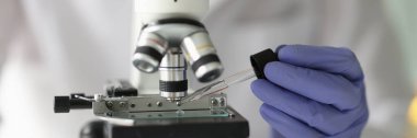 Close-up of chemist lab assistant looking at test sample using microscope. Quality control and laboratory research concept