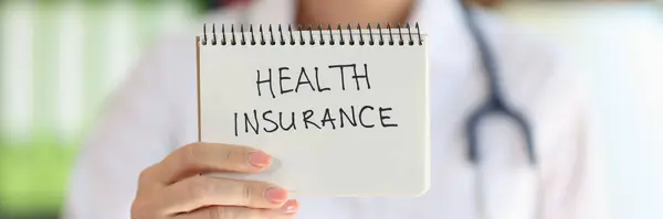 stock image Close-up of female doctor showing notepad with words health insurance. Health worker recommends to buy health insurance