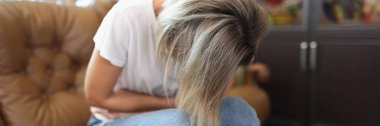 Portrait of female sitting on sofa, touching belly and writhing in pain. Stomachache, menstrual pain, gastritis or diarrhoea. Healthcare medical concept