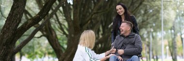 Friends kidding and laughing while walking in park, one male friend sitting in wheelchair. Friendship and support for disabled people concept.
