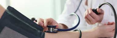 Doctor uses sphygmomanometer with stethoscope to check blood pressure of patient in hospital. Close up of blood pressure measuring, health care concept.
