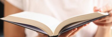Woman holding open book in her hands close up, shallow depth of field. Concept of searching information, learning and reading novels.