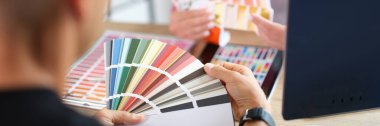 Manager and client holding color swatch cards while sitting at table in design studio. Client chooses colors for renovation of his home.