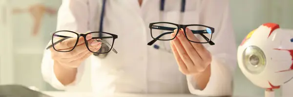 眼科医生坐在诊所的办公桌前 手里拿着不同的眼镜 医生推荐她的病人配眼镜 — 图库照片